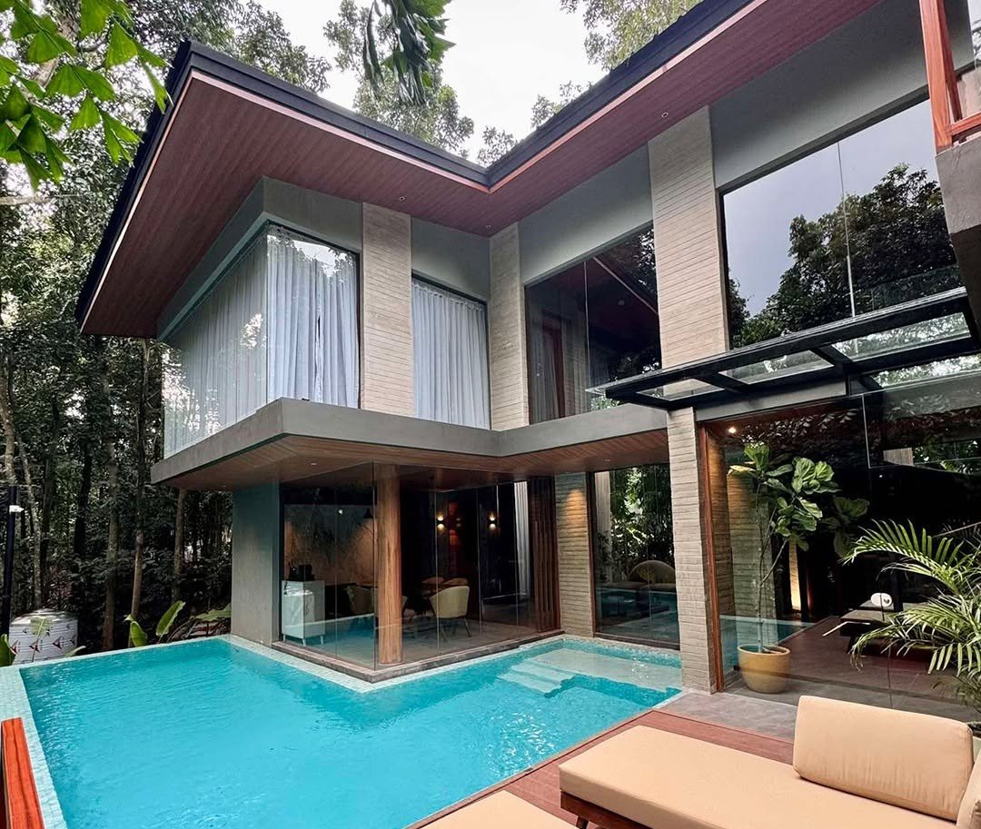 Two-storey villa with a turquoise pool, timber soffits, and glass walls set in tropical greenery
